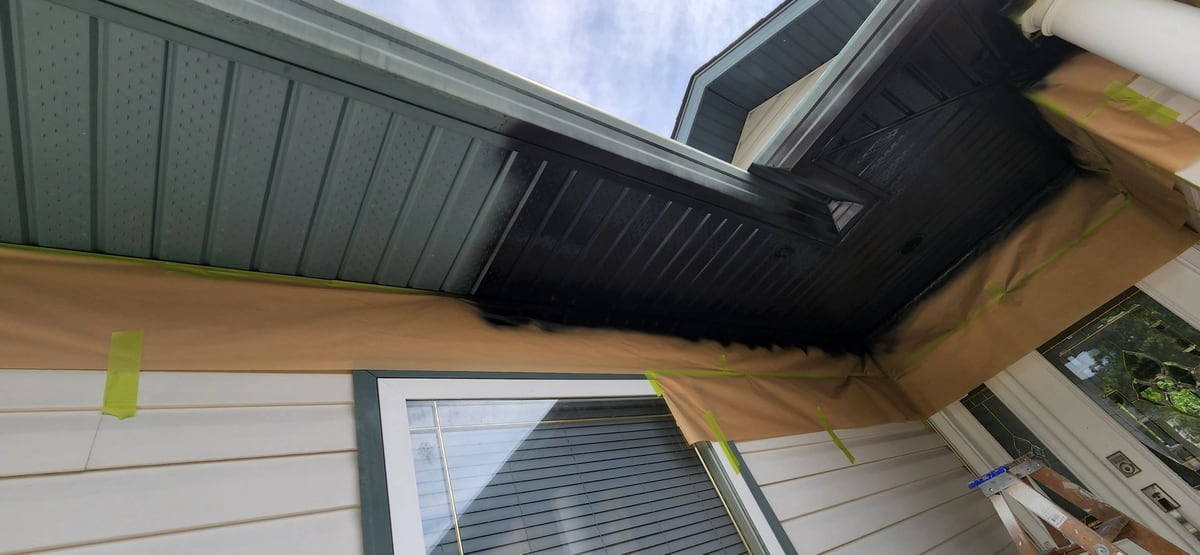 Before: Soffits rolled dark brown while masking paper protects the siding and windows below.